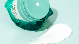 All Day duo moisturizer posed with jelly, next to a swatch of moisturizer on green background.