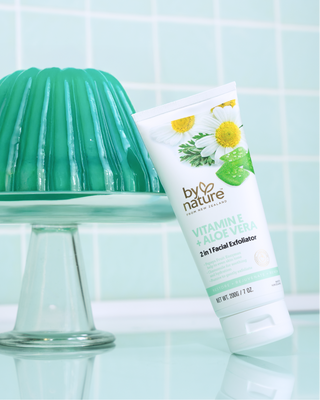 Tube of By Nature facial exfoliator leaning on green jelly on a stand, against a light green tiled wall.