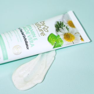 Tube of By Nature aloe vera + Vitamin E facial exfoliator with a smear of product on a light blue background