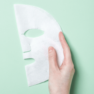 Hand holding a white face mask with a  a light green background