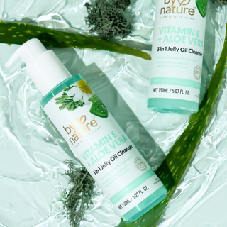Two bottles of By Nature Vitamin E and Aloe Vera skincare product on a textured green background with Aloe Vera leaves and  algae