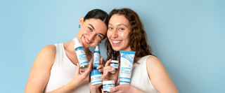 Two smiling women holding By Nature  skincare Hyaluronic Acid products against a solid light blue background.